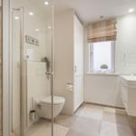 Badezimmer mit Dusche, WC und Waschbecken. Fenster mit Rollladen und Pflanze.