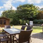 Garten mit Tisch, Stühlen, Holzhaus und Blumen.