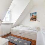 Zimmer mit zwei Betten, Fenster, Heizkörper und Wandbild.