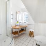 Badezimmer mit Dusche, Waschbecken und Toilette unter schrägem Dach