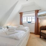 Schlafzimmer mit Dachschrägen, Bett, Sessel und TV.