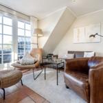 Wohnzimmer mit braunen Ledermöbeln, Glas-Tisch und großen Fenstern.