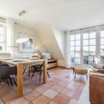 Essbereich mit Tisch, Stühlen und Fenstern. Wohnbereich mit Ledersofa und Sicht auf Balkon.