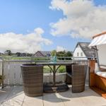 Terrasse mit Tisch, Stühlen und Sonnenschutz. Blick auf Wohnhäuser und Grünflächen.