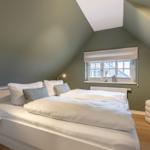 Bedroom with sloped ceiling, bed, window, and stool.