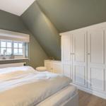 Bedroom with sloped ceiling, white wardrobe, and bed. Window with roller blind and TV.