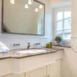 Bathroom with sink, mirror, and window. Towels and care products on the countertop.