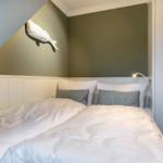 Bedroom with double bed, wall lamp, and whale decoration.