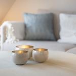 Three gold-rimmed cups sit on a round table in front of a sofa with cushions.