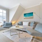 Living room with sofa, two chairs, and table under sloped ceiling with window.