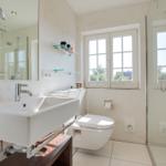 Badezimmer mit Dusche, Waschbecken und Toilette. Fenster mit Blick auf Grün.