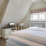 Schlafzimmer mit Dachbodenfenster, weißem Bett und Fernseher auf Schrank.