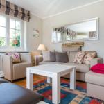 Wohnzimmer mit Sofa, Sessel und Tisch. Fenster, Spiegel und Teppich sind sichtbar.