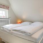 Schlafzimmer mit Doppelbett, Fenster und Stehlampe.