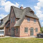 Red brick house with thatched roof and garden area with table and umbrella.