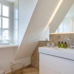 Bathroom with sink, mirror and window. Sloped ceiling and stone wall.