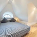 Bedroom with sloped ceiling, wooden floor, and round window.
