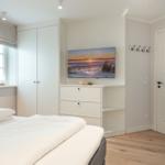 Bedroom with white bed, wardrobe, and TV mounted on the wall.