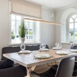 Dining room with wooden table, black chairs, and two windows overlooking outside.