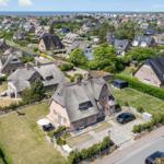 Thatched-roof house with garden. View of coastal town with sea in background.