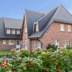 Red brick house with dark gabled roof and rose bushes in the foreground.