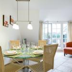 Dining table with six chairs and glass top. Background: window and armchair.