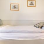 A bed with white sheets and pillows. Two framed pictures hang on the wall.