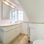 Bathroom with sink, mirror, and shower under sloped ceiling.
