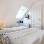 Room with two beds, sloped ceiling, skylight, and TV mounted on wall.