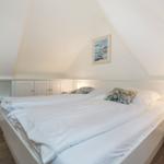 Bedroom with double bed, nightstand, and wall art under sloped ceiling.