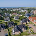 Aerial view of residential area with houses, gardens, and ocean in background.
