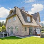 House with thatched roof, terrace, and garden. White windows and wooden doors.