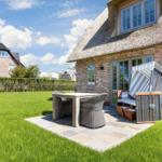 House with thatched roof, terrace, and garden. Outdoor table, chairs, and lounge chair.
