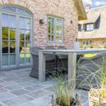 Terrace with table and chairs in front of brick house with sliding doors.