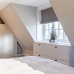 Bedroom with sloped ceiling, window, and white cabinets.