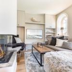 Living room with fireplace, sofa, and wooden table. Arched window and decorative elements.