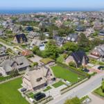 Aerial view of a coastal town with thatched-roof houses and green lawns near the sea.