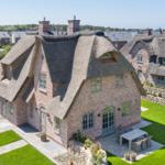 House with thatched roof, garden, and terrace with table and chairs.