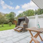 Terrasse mit Liegestuhl, Tisch und Stühlen. Hinterhof mit Grünfläche und weißer Hecke.
