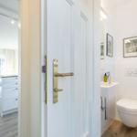 Hinter einer weißen Tür ist ein Badezimmer mit Toilette und Waschbecken sichtbar.