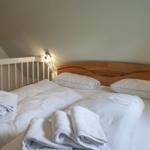 Double bed with white linens and folded towels under a sloped ceiling.