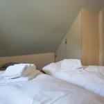 Two beds with white bedding and folded towels under sloped ceiling walls.