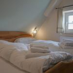 Double bed with white bedding and folded towels under sloped ceiling.