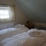 Two beds with white bedding and towels under a sloped ceiling window.