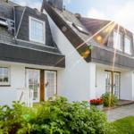 White villa with dark roof and multiple entrances. Garden with flowers and grass.