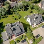 Aerial view of several houses with green lawns and parked cars.