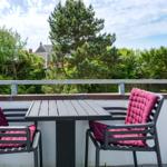 Terrace with table and two chairs with purple cushions. View of trees and sky.