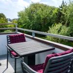 Terrace with table and two chairs with cushions. View of green trees and a river.
