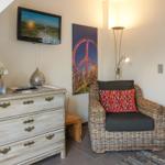 Living room with TV, dresser, and armchair. Wall art and floor lamp visible.