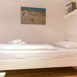 A bed with white bedding, wall picture, and shelf on the wall.